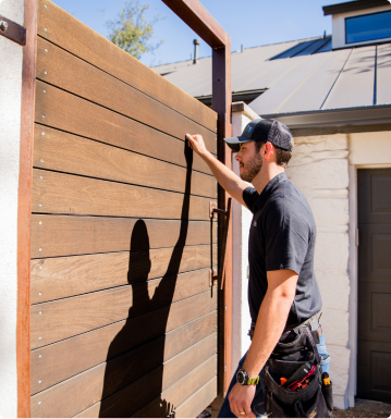 an hvac technician knocks on a wooden gate on the side of someone's home 
