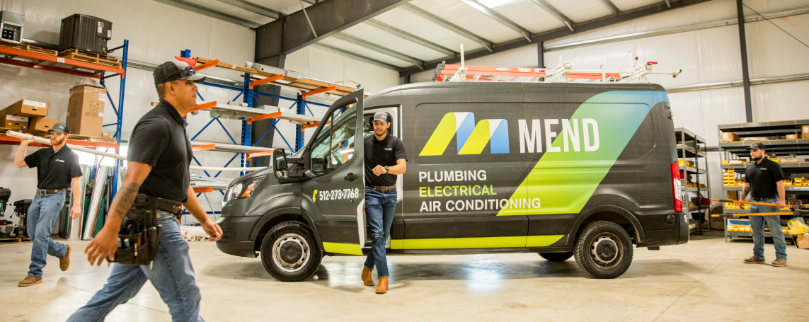 A warehouse with a work van that says Mend on the side with a technician walking out of the van and other technicians working in the background
